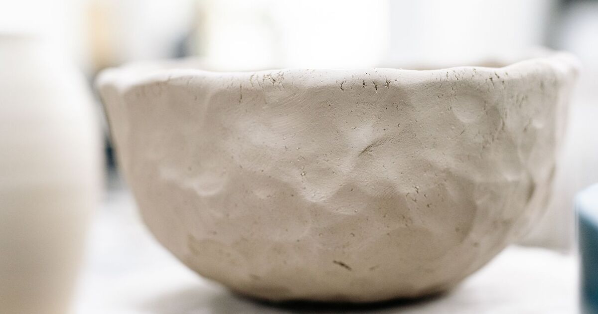 Bol en argile artisanale brute posé sur une étagère en bois sombre, texture rugueuse en gros plan