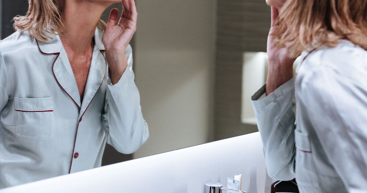 Femme mature observe son visage dans le miroir de la salle de bain pendant sa routine du matin