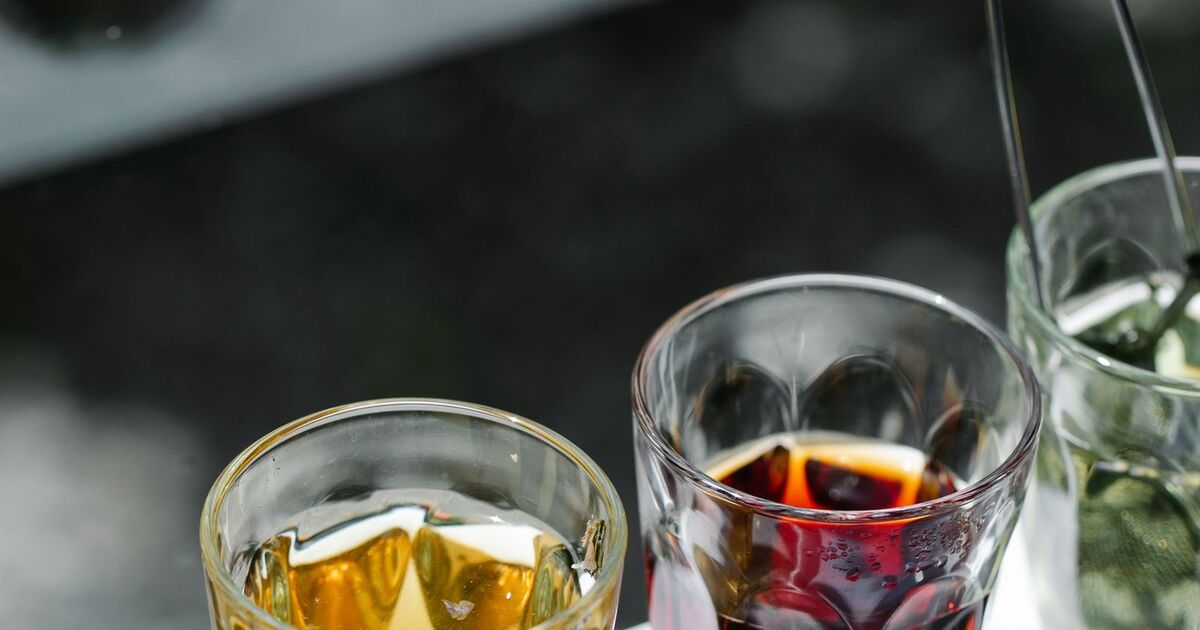 Mains tenant un verre de tisane fumante, plantes et épices séchées posées autour sur une table en bois